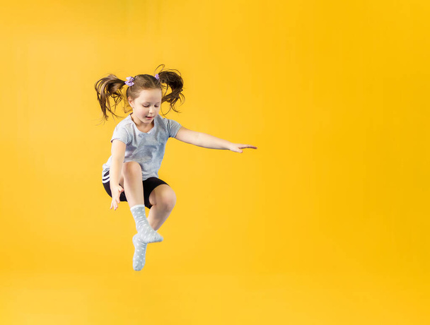 Happy little girl jumping on a yellow background - Photo, image