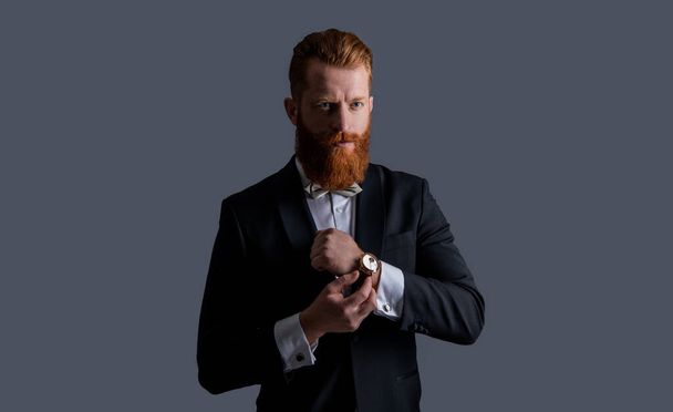 man studio shot in tuxedo and wrist watch. man wearing elegant wrist watch and tuxedo. tuxedo fashion. handsome bearded man in tuxedo with wrist watch isolated on grey background. - Photo, image