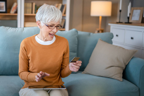 Jedna starší žena babička sedět doma používat kreditní nebo debetní karty pro on-line nakupování prohlížet internetové obchody nakupování věci na prodej slev skuteční lidé kopírovat prostor použít digitální tablet - Fotografie, Obrázek