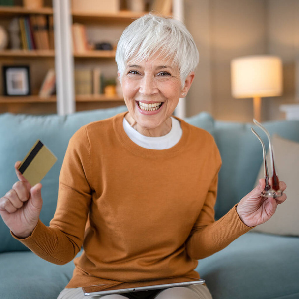 Egy érett idős nő nagymama ül otthon hitel- vagy betéti kártya online vásárlás böngészés internetes áruházak vásárol dolgokat akciós áron valódi emberek másolni tér használata digitális tabletta - Fotó, kép