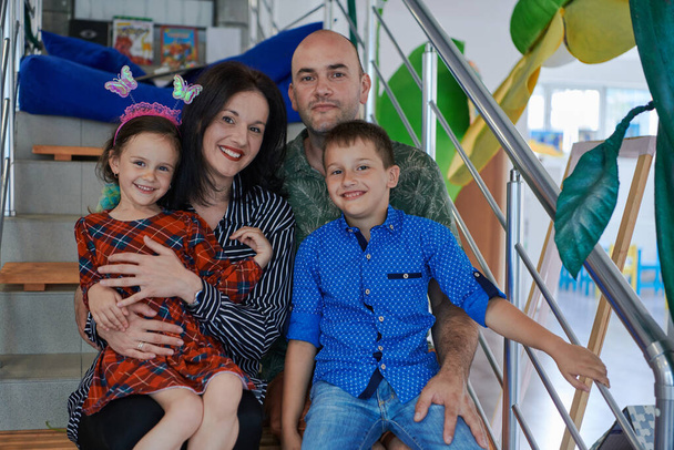 Portrait of a happy family. Photo of parents with children in a modern preschool classroom. Selective focus . High quality photo - Fotografie, Obrázek