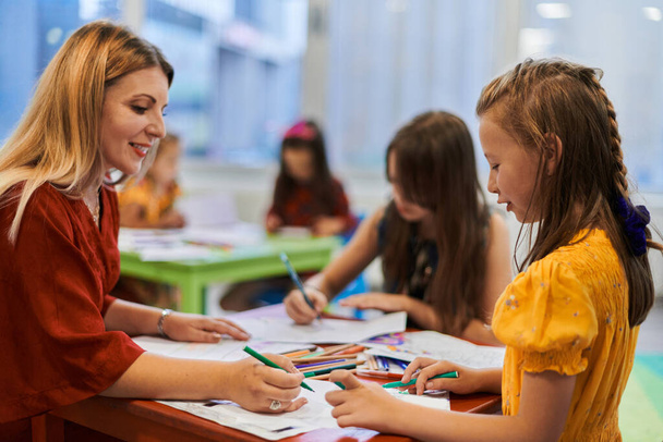 Creative kids during an art class in a daycare center or elementary school classroom drawing with female teacher - Фото, зображення
