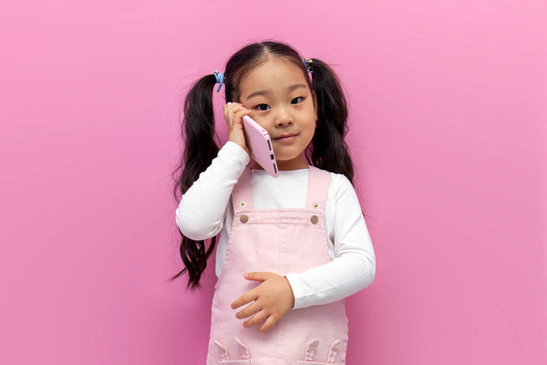 little asian girl in pink sundress talking on the phone on pink isolated background, korean preschool child communicates on mobile phone - Fotoğraf, Görsel