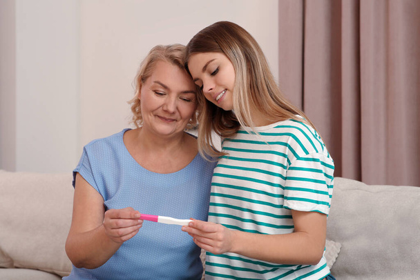 Young woman showing her mother pregnancy test at home. Grandparent reaction to future grandson - Foto, Imagen