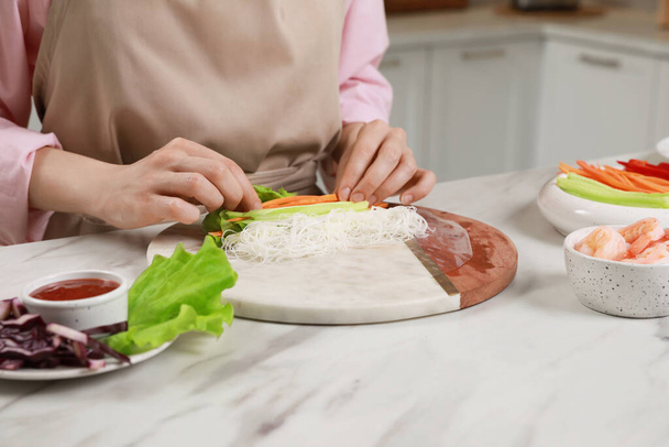 Making delicious spring rolls. Woman wrapping ingredients into rice paper at white marble table, closeup - Valokuva, kuva