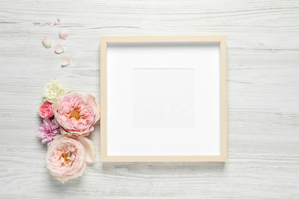 Empty photo frame and beautiful flowers on white wooden table, flat lay. Space for design - Valokuva, kuva