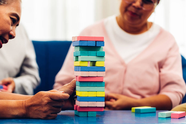 Senior people playing a wooden block tower, risk and strategy of project management. Concept of business risk with domino blocks. Older People playing jenga block removal game on table at home - Φωτογραφία, εικόνα