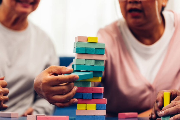 Senior people playing a wooden block tower, risk and strategy of project management. Concept of business risk with domino blocks. Older People playing jenga block removal game on table at home - 写真・画像