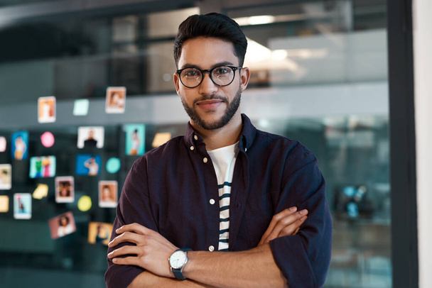 This is where business magic happens. Cropped portrait of a handsome young businessman wearing spectacles and standing alone in his office with his arms folded - Photo, Image