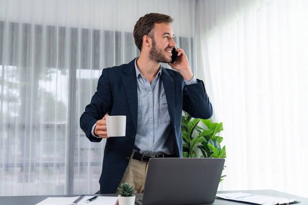 Fleißiger und fleißiger Geschäftsmann, der an seinem Laptop arbeitet, während er mit Kunden auf seinem Mobiltelefon spricht und den modernen Multitasking-Büroarbeiterlebensstil präsentiert. Einheit - Foto, Bild
