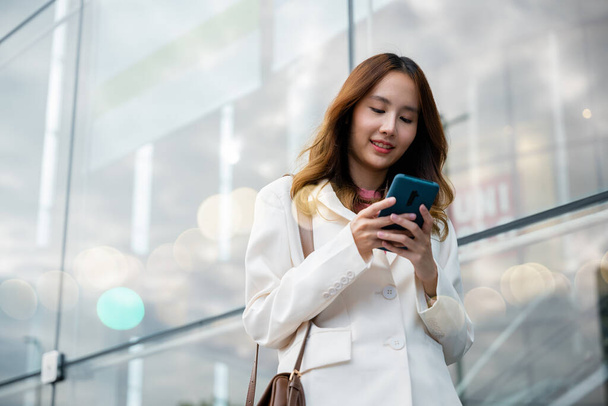 Portrait successful business woman smiling holding smartphone using app chat online in morning, Asian businesswoman typing text on mobile phone standing outdoors street front building near office - Photo, image