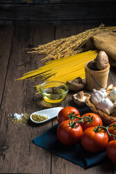 Close up Diverse ingrediënten voor het maken van spaghetti zoals spaghetti, tomaten, champignons, oregano en diverse kruiden op een houten tafel, met kopieerruimte. - Foto, afbeelding