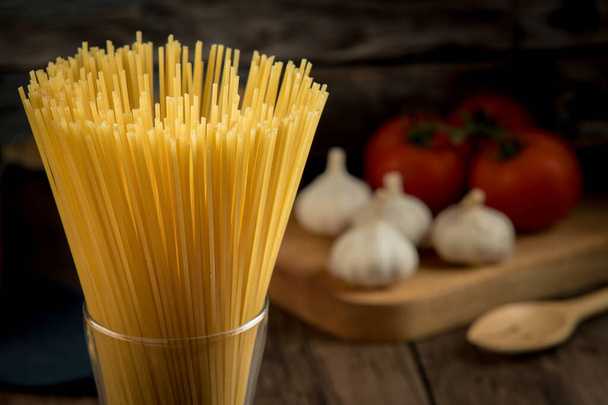 Varios ingredientes para hacer espaguetis como espaguetis en un vaso, tomates, champiñones, orégano y varios condimentos colocados en una mesa de madera. - Foto, Imagen