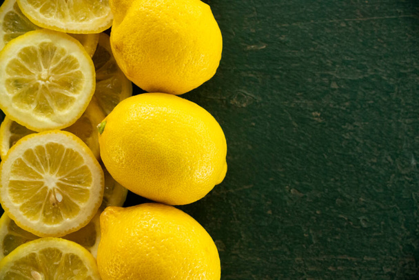 fila de limones enteros y cortados en rodajas creando un borde sobre un fondo de textura rústica verde - Foto, Imagen
