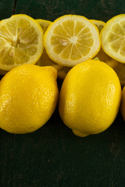 row of whole and sliced lemons creating a border on a green rustic textured background - Foto, Imagen