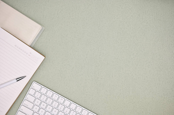 緑の背景に白いキーボード、ペン、ノートブック、空のスペースと現代の最小限のオフィスワークスペース。トップビュー - 写真・画像