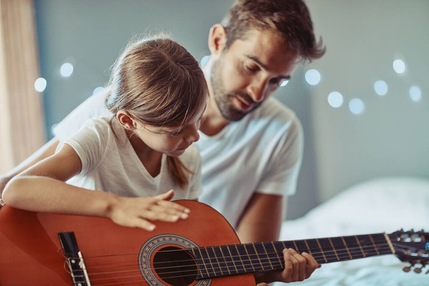 Man, girl and kid in guitar teaching and learning at home, bonding with love and creativity. Family, father and daughter learn to play musical instrument, focus in lesson and music education help. - Foto, afbeelding