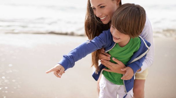 Mother, child and pointing outdoor at beach for family travel or holiday in summer with a smile and fun. A woman and kid or son playing together on vacation at sea with love, care and happiness. - Φωτογραφία, εικόνα