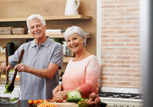 Főzés, segítség és portré az idős pár a konyhában a saláta, a szerelem és a táplálkozás. Boldog, mosolygós és nyugdíjas idős férfi és nő vágás zöldségek otthon élelmiszer, vacsora és recept. - Fotó, kép