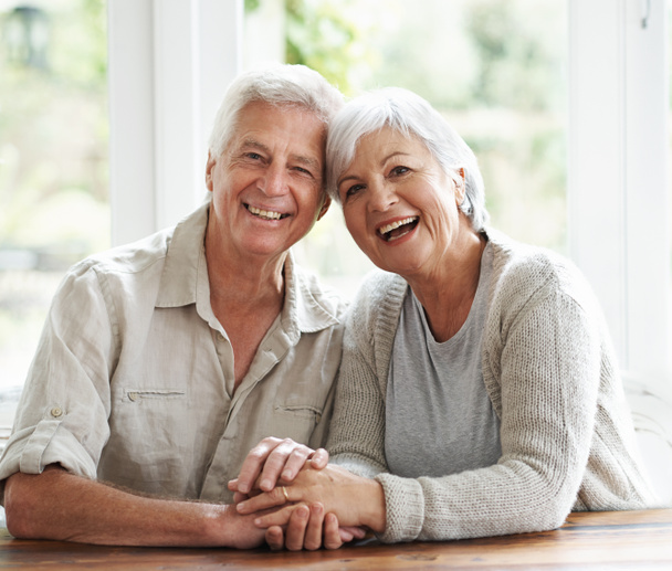 Portré, nevetés és idős pár fogja egymás kezét a szerelemért, gondoskodásért és pihenésért otthon. Arca boldog öregember, nő és segítő kéz a bizalom, támogatás és hűség partner nyugdíjba. - Fotó, kép