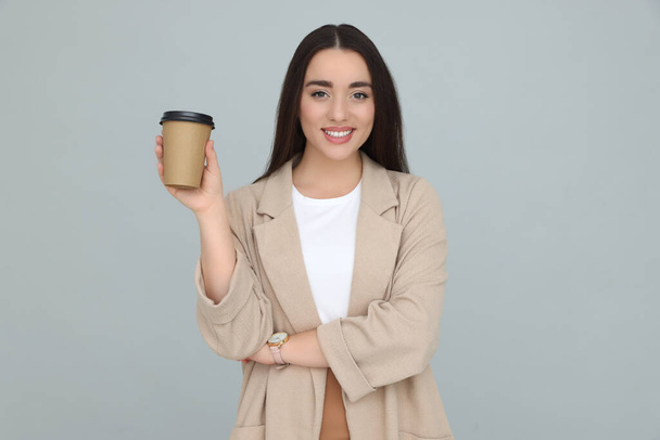 Young female intern with cup of drink on grey background - Foto, imagen