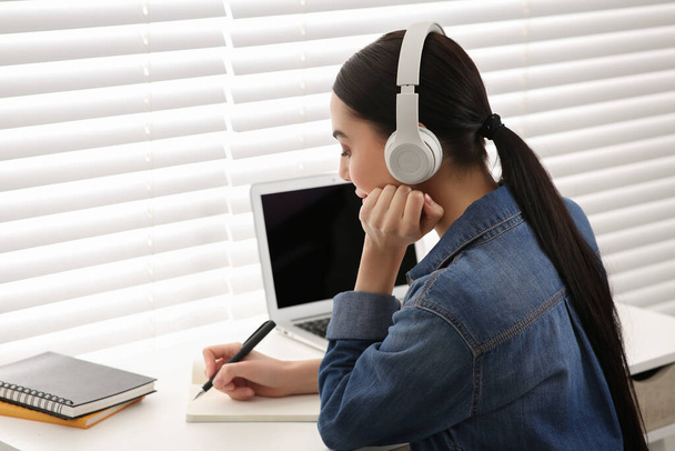 Online translation course. Student in headphones writing near laptop indoors - Valokuva, kuva