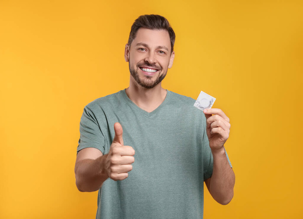 Happy man with condom showing thumb up on orange background - Foto, imagen