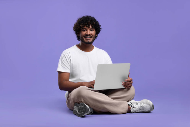 Happy man with laptop on purple background, space for text - Фото, изображение