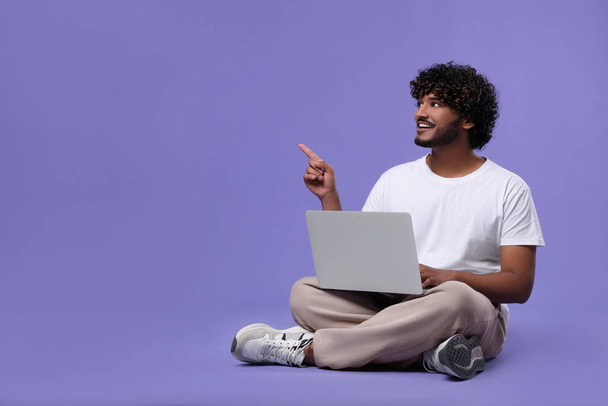 Happy man with laptop on purple background, space for text - Fotó, kép