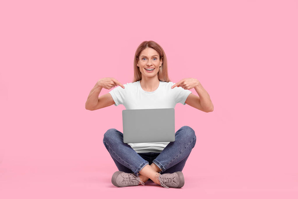 Happy woman pointing on laptop against pink background - Фото, зображення
