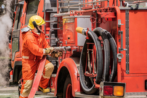 With focused precision, the firefighter securely plugs the fire hose into the designated outlet on the fire truck ensuring a reliable connection for immediate use in aiding fire victims. - Photo, Image