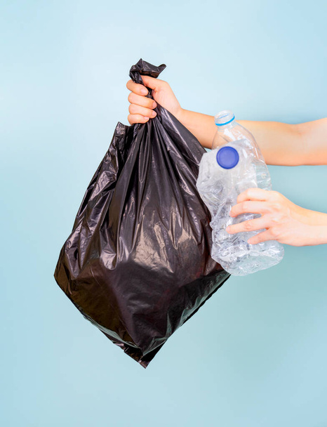 une main tenant un sac en plastique rempli de bouteilles en plastique, l'autre tenant une bouteille en plastique déchets.isolé sur fond bleu, concept de déchets plastiques, tri des déchets et gestion des déchets - Photo, image