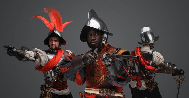Ritratto di gruppo multietnico di tre conquistatori con armature in acciaio e fucili a pietra focaia. - Foto, immagini