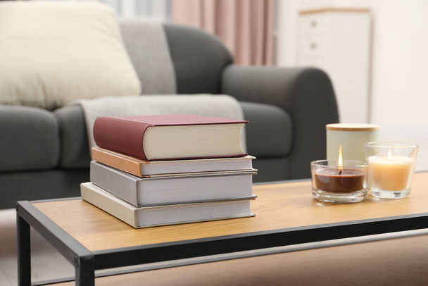 Books and burning candles on wooden table in living room - Foto, imagen