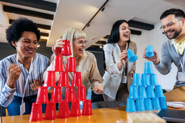 Group of young business people playing, building towers from plastic cups, two teams, blue and red. Teambuilding activity. - Фото, изображение