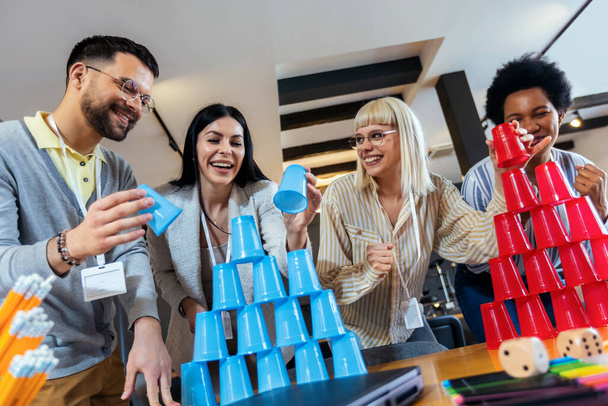 Grupo de jóvenes empresarios jugando, construyendo torres de vasos de plástico, dos equipos, azul y rojo. Actividad de Teambuilding. - Foto, Imagen