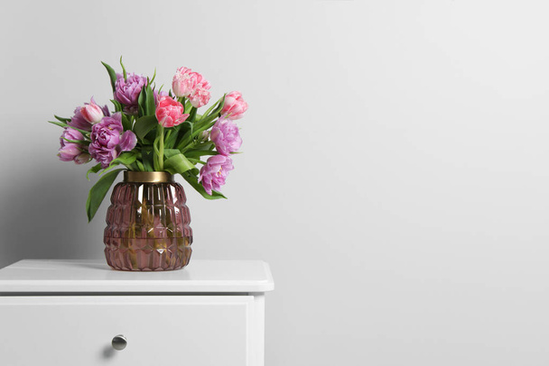Beautiful bouquet of colorful tulip flowers on white bedside table near white wall, space for text - Фото, зображення