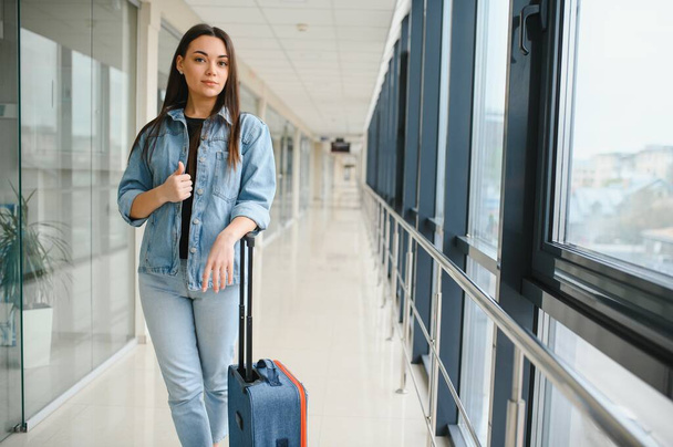 Молодая женщина тащит чемодан в терминале аэропорта. Копировальное пространство. - Фото, изображение