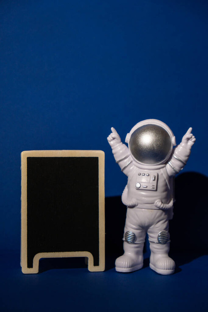 Plastic toy astronaut with blackboard template mock up for your text on colorful blue background Copy space. Concept of out of earth travel, private spaceman commercial flights. Space missions and - 写真・画像