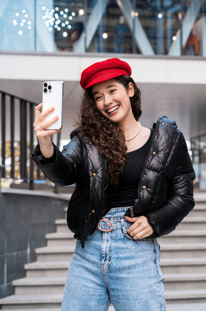 若いです笑顔女性ブロガーインフルエンサーで赤い帽子で自分自身を撮影スマートフォン - 写真・画像