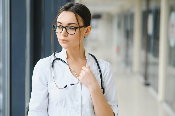 Portrait of young female doctor standing in hospital corridor. Caucasian woman working in nursing home - Φωτογραφία, εικόνα