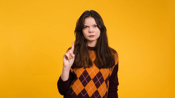 Serious young woman showing sign of refusal on a yellow background - Photo, Image
