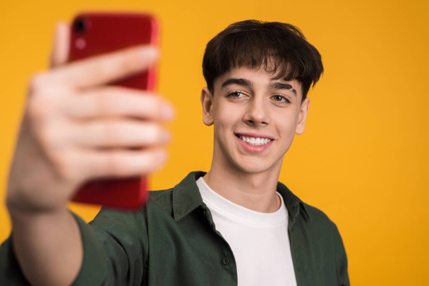 Young man talking while filming himself on the phone on a yellow background - Φωτογραφία, εικόνα