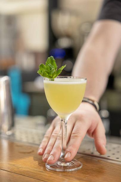 De barman versierde zijn gele cocktail met munt. restaurant serveert - Foto, afbeelding