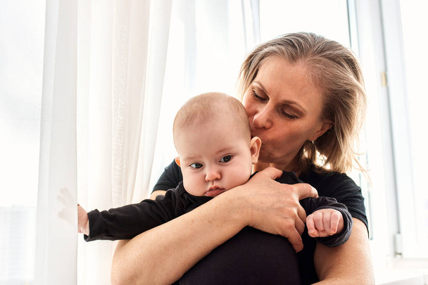 Мама обіймає і цілує свою дитину в яскравій дитячій кімнаті. Мама обережно тримає дитину на руках. Щасливе дитинство. - Фото, зображення