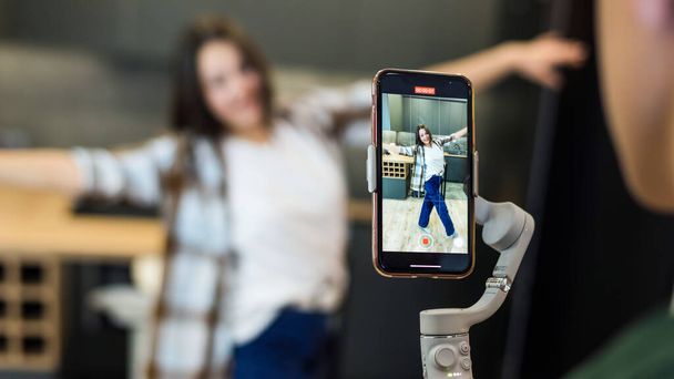 Une personne enregistrant une jeune blogueuse danseuse influenceuse sur smartphone sur un stabilisateur dans un studio - Photo, image