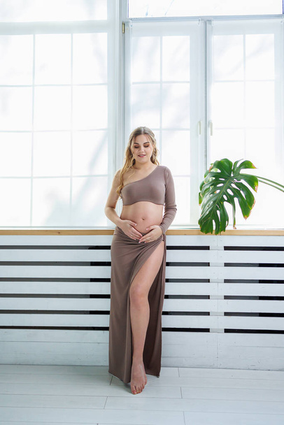 Una hermosa mujer embarazada en un top y falda abraza su vientre. Mujer embarazada con estilo - Foto, imagen