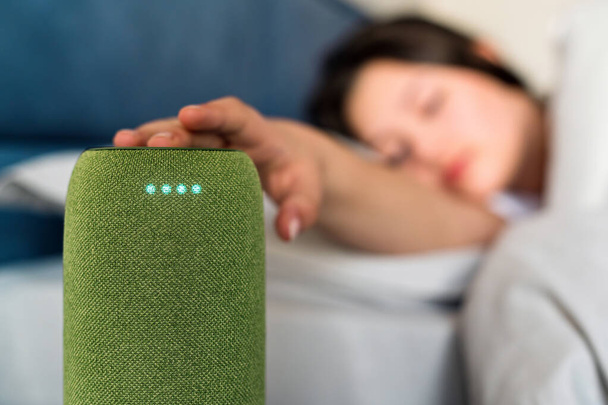 Спящая женщина выключает будильник на переносном беспроводном динамике с 4 светящимися диодами - Фото, изображение