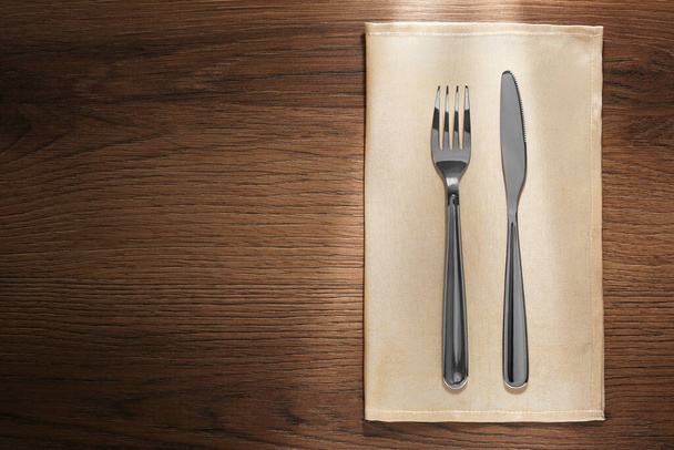 Shiny fork, knife and napkin on wooden table, top view. Space for text - Фото, зображення