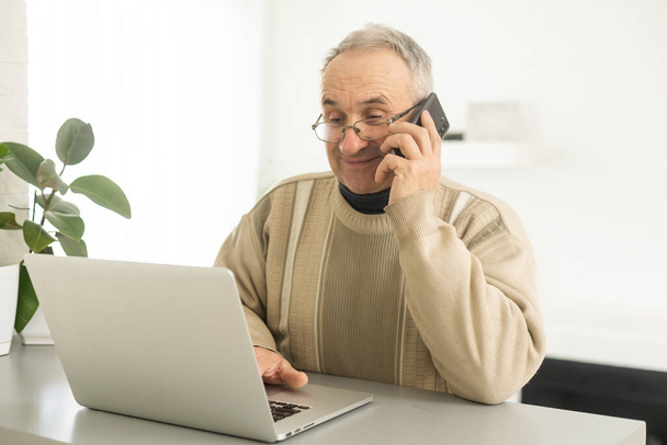 senior man looking at laptop and phone calling at home - Фото, изображение